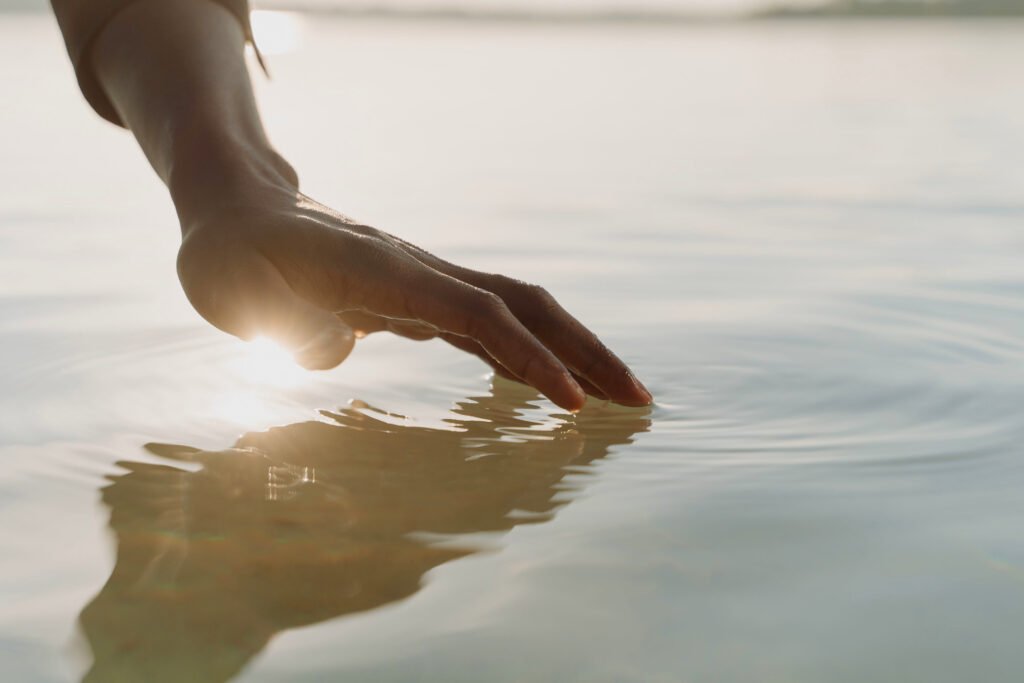 Dott. Cristiano Pedersini — Metafora visiva del contatto emotivo in psicoterapia: una mano sfiora delicatamente la superficie dell'acqua creando cerchi di luce e onde concentriche, simbolo dell'ascolto profondo, della cura e della connessione con il proprio mondo interiore. dell'accarezzare le proprie emozioni per iniziare il viaggio di consapevolezza.