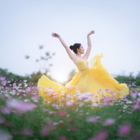 Dott. Cristiano Pedersini - Donna in abito giallo che danza libera in un prato fiorito, simbolo di riscatto, vitalità e piena armonia con il proprio corpo, supporto per il benessere psicofisico e disagio corporeo