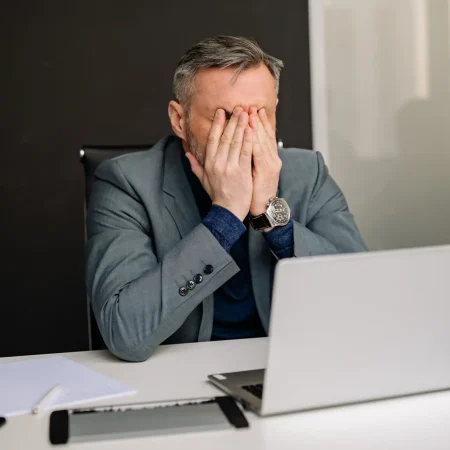 Dott. Cristiano Pedersini - Uomo in abito formale che si copre il volto al computer, simbolo di stanchezza profonda e necessità di fermarsi, supporto per lo stress lavorativo